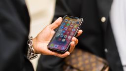 A guest wears silver bracelet, holds in his hand an iPhone unlocked on the application screen, outside Officine Générale, during Paris Fashion Week - Menswear Spring/Summer 2022, on June 25, 2021 in Paris, France.