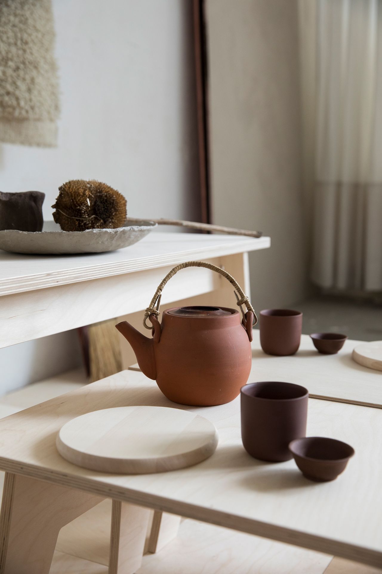 An earthern tea pot sits on a sleek wooden table designed by Woodchuck, styled by Tinta.
