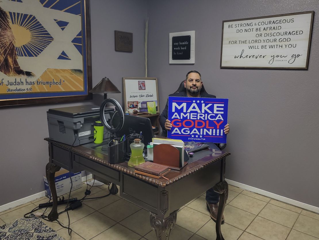 Pastor Luis Cabrera holds a "Make America Godly Again" sign in his office on October 27, 2022. 