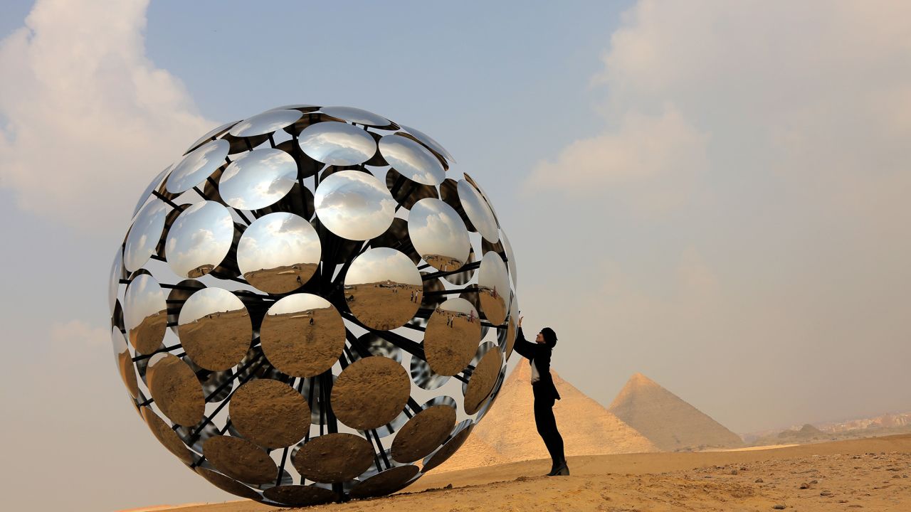 Visitors pose by the "Orb: Under the same Sun" installation by Madrid-based international artist SpY at the Giza pyramids necropolis during the second edition of the Art D'Égypte exhibition "Forever is Now" on October 27 in Giza, Egypt.