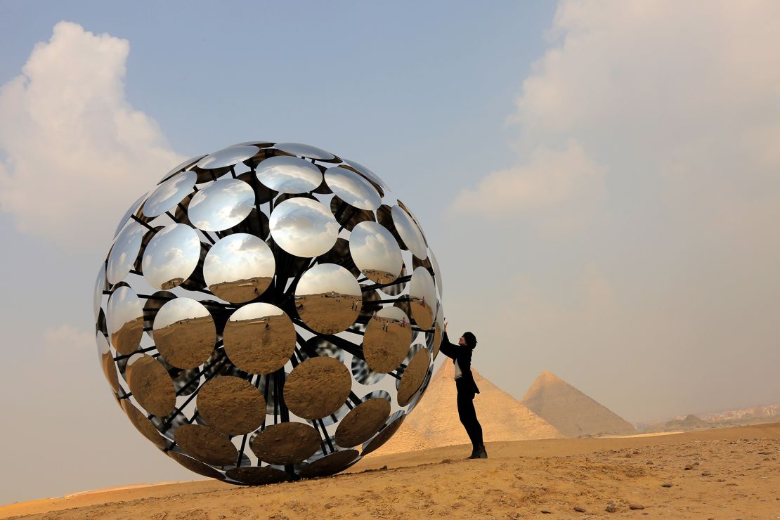 Visitors pose by the "Orb: Under the same Sun" installation by Madrid-based international artist SpY at the Giza pyramids necropolis during the second edition of the Art D'Égypte exhibition "Forever is Now" on October 27 in Giza, Egypt. 