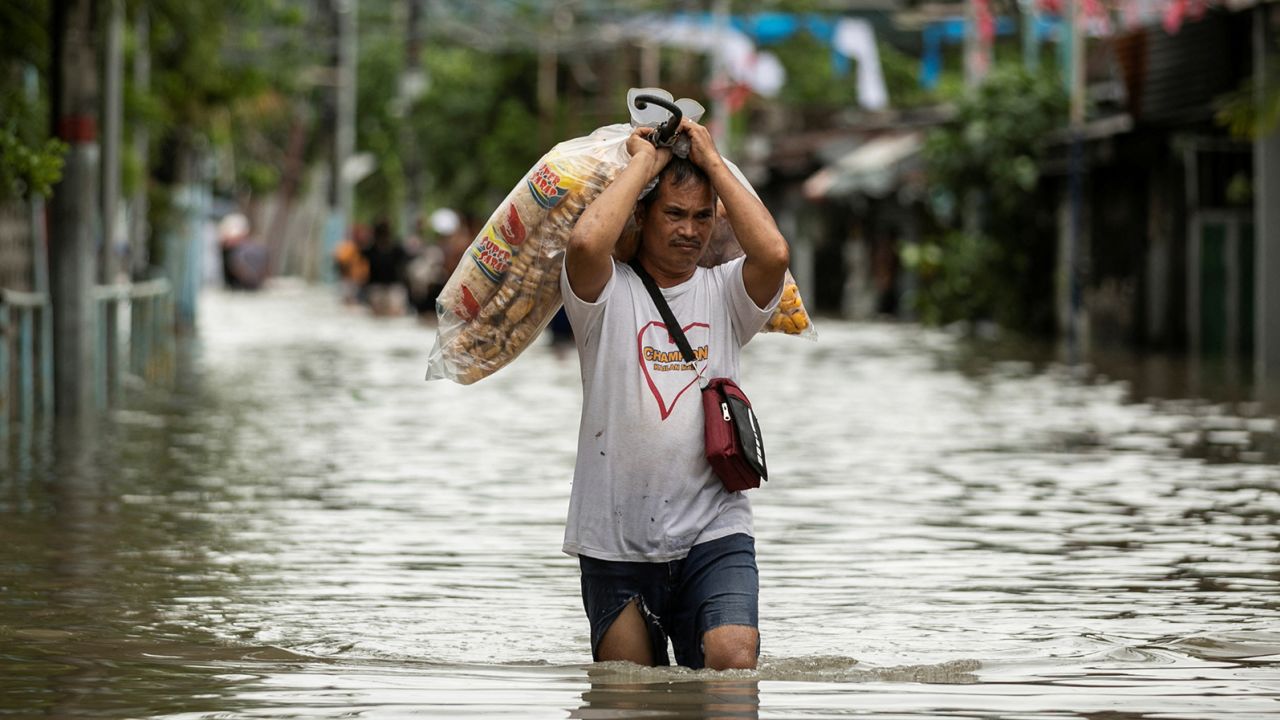 A vendor carries food products as he wades through a flooded street following heavy rains brought by tropical storm Nalgae over the weekend. 