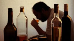 silhouette of anonymous alcoholic person drinking behind bottles of alcohol.