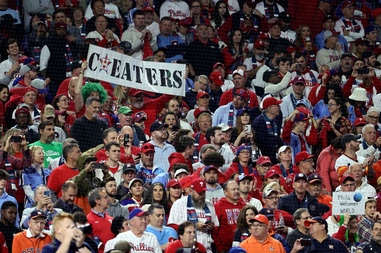 Phillies fans hold up a "cheaters" sign with the Astros' logo on Tuesday night. The Astros won the World Series in 2017, but many baseball fans consider that title tainted because of a cheating scandal. Major League Baseball found that the team had illegally created a system that decoded and communicated the opposing teams' pitching signs during their championship season, leading Astros owner and chairman Jim Crane to fire manager AJ Hinch and general manager Jeff Luhnow.