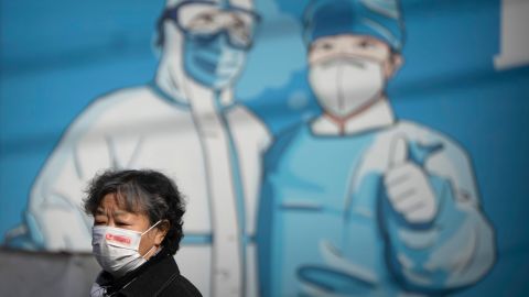 A woman wearing a face mask walks past a mural depicting epidemic control workers in protective suits in Beijing, Tuesday, Nov. 1, 2022. 