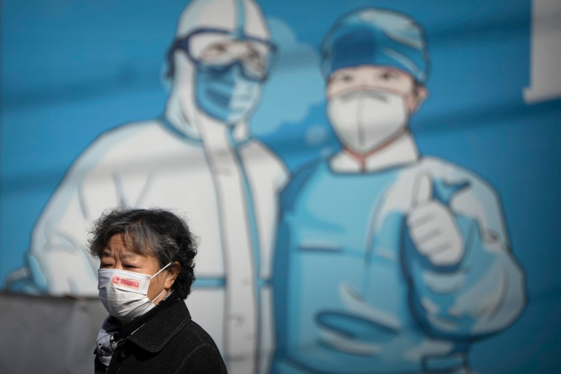 A woman wearing a face mask walks past a mural depicting epidemic control workers in protective suits in Beijing, Tuesday, Nov. 1, 2022. 