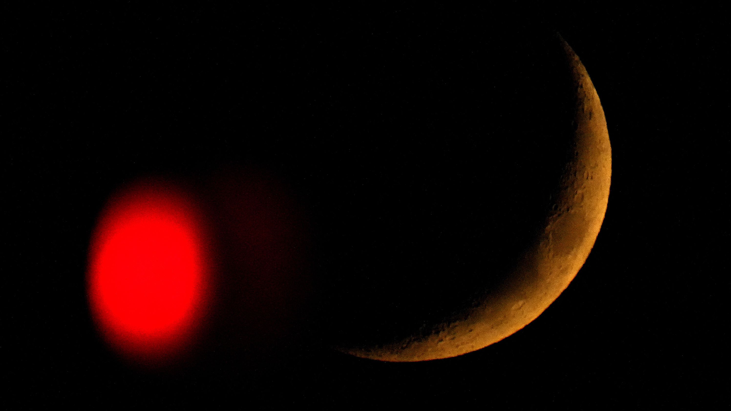 The crescent moon sets behind a stop light in Overland Park, Kansas, on Friday, October, 28.