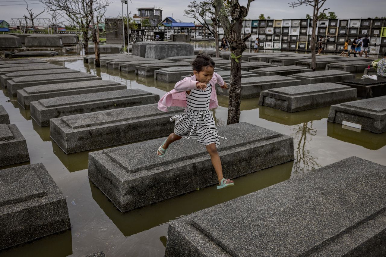 A girl jumps across tombs at a flooded cemetery following Tropical Storm Nalgae as Filipinos mark All Saints' Day on Tuesday, November 1, in Masantol, Philippines.