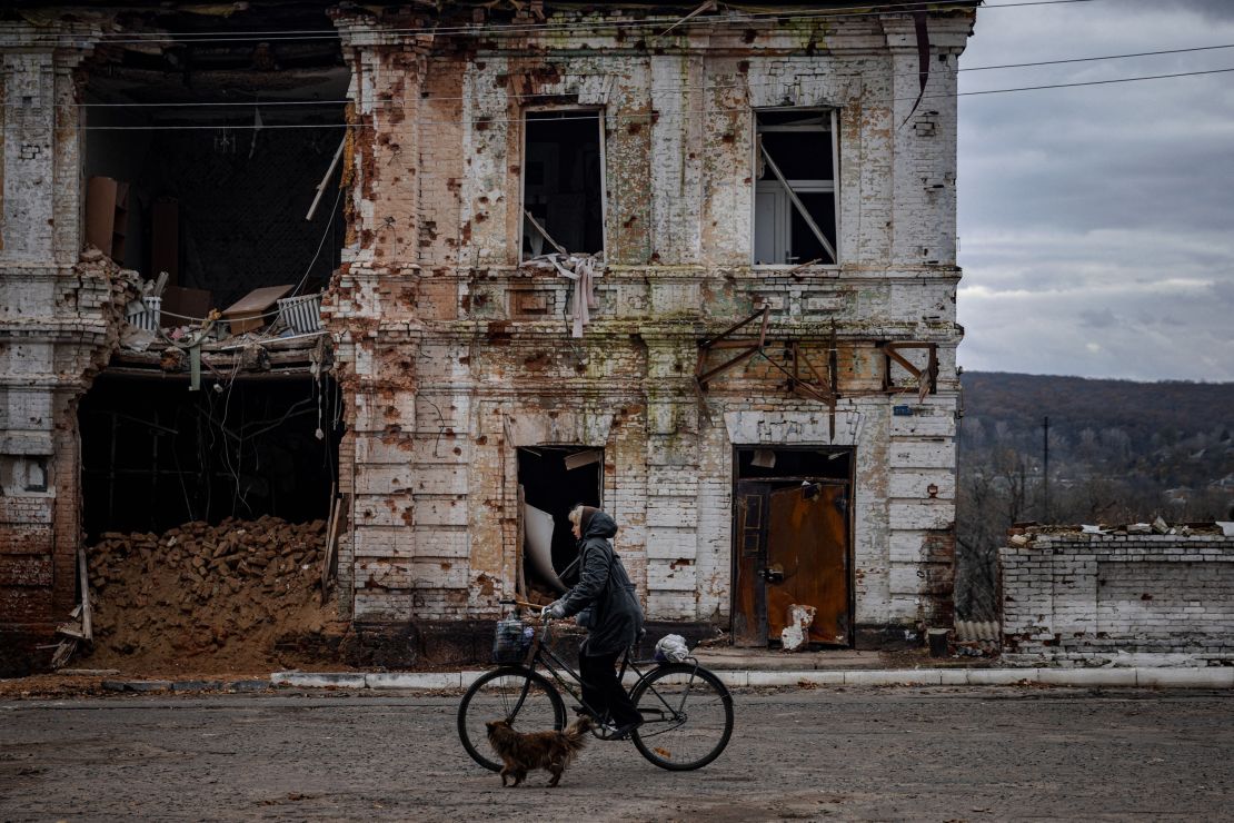A woman rides a bicycle past a damaged building in the town of Kupiansk on November 3, 2022, Kharkiv region, amid the Russian invasion of Ukraine.