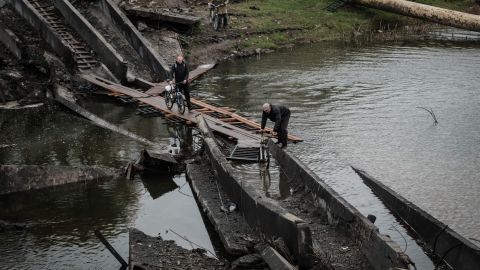 2022 年 10 月 11 日、ドネツク地方の最前線の町バフムートで、破壊された橋を自転車で渡る男性たち。