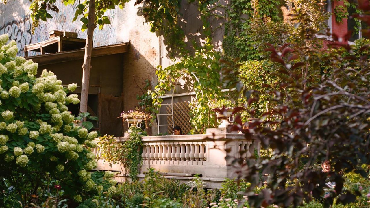 A woman reads on the balcony, which overlooks a rose bush, hydrangea tree and various flower beds in Elizabeth Street Garden.