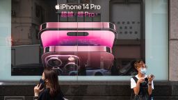 A pedestrian using a smartphone walks past an American multinational technology company, Apple iPhone 14 Pro advertisement in Hong Kong. 