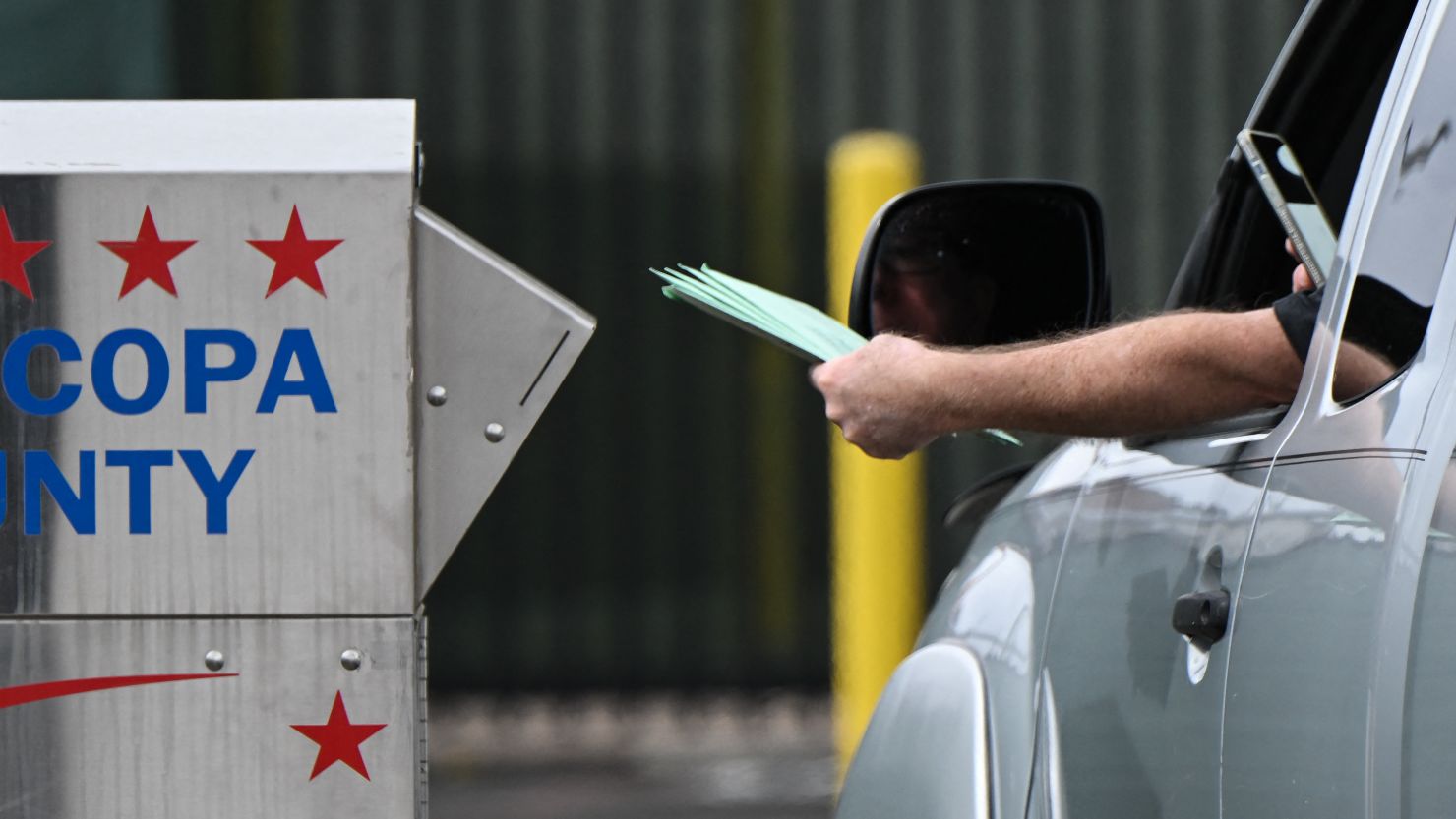 A driver uses a smartphone as they drop off multiple ballots into a ballot drop box for early voting outside of the Maricopa County Tabulation and Election Center ahead of the Arizona midterm elections in Phoenix, Arizona on November 3, 2022. (Photo by Patrick T. FALLON / AFP) (Photo by PATRICK T. FALLON/AFP via Getty Images)