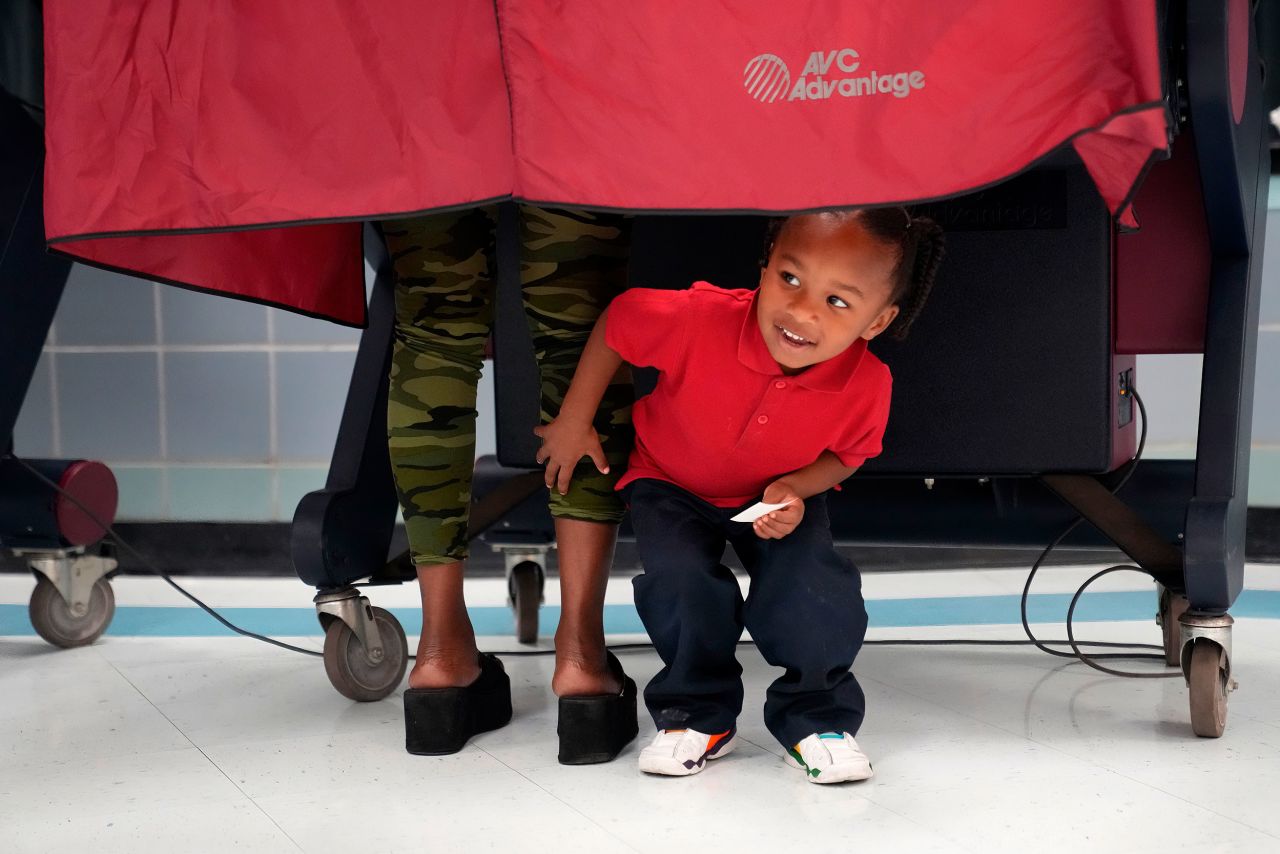 Kash Strong, 3, peeks out from under the curtain of a voting booth as his mother, Sophia Amacker, casts her vote in New Orleans.