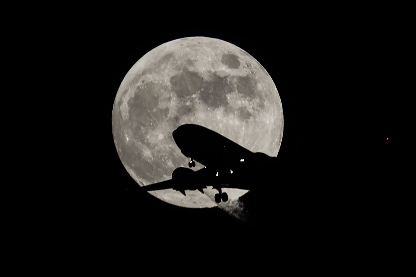 A passenger plane flies past the full moon before landing at San Francisco International Airport, as seen from Foster City, California, on November 7.