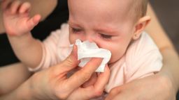 A small, sick, crying child, whom the mother wipes with a paper towel 