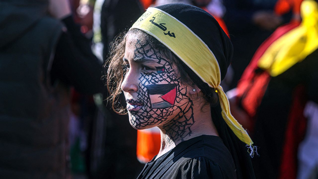 A girl with face-paint depicting the Palestinian flag looks on as others gather with flags of the Fatah movement during a rally to commemorate the 18th anniversary of the death of Palestinian leader Yasser Arafat, in Gaza City on Thursday.
