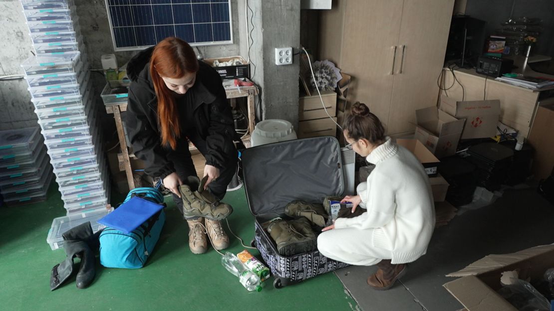 Twenty-one-year-old Roksolana, left, tries on her new boots while Kseniia Drahanyuk, the co-founder of the Zemlyachki NGO, helps her fill a suitcase with all kinds of items.