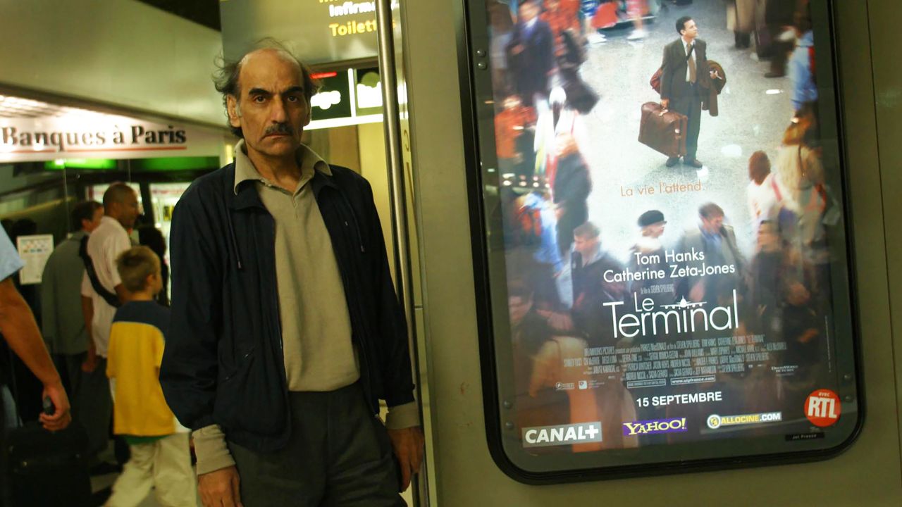 Mehran Karimi Nasseri standing next to a poster of Steven Spielberg's movie "The Terminal" which was loosely based on his life stranded in Charles de Gaulle Airport.