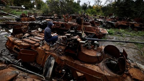 A volunteer uses his mobile phone as he sits on the top of a destroyed Russian armoured vehicle in the recently liberated town of Izium, in Ukraine's northeastern Kharkiv region, on September 27, 2022.