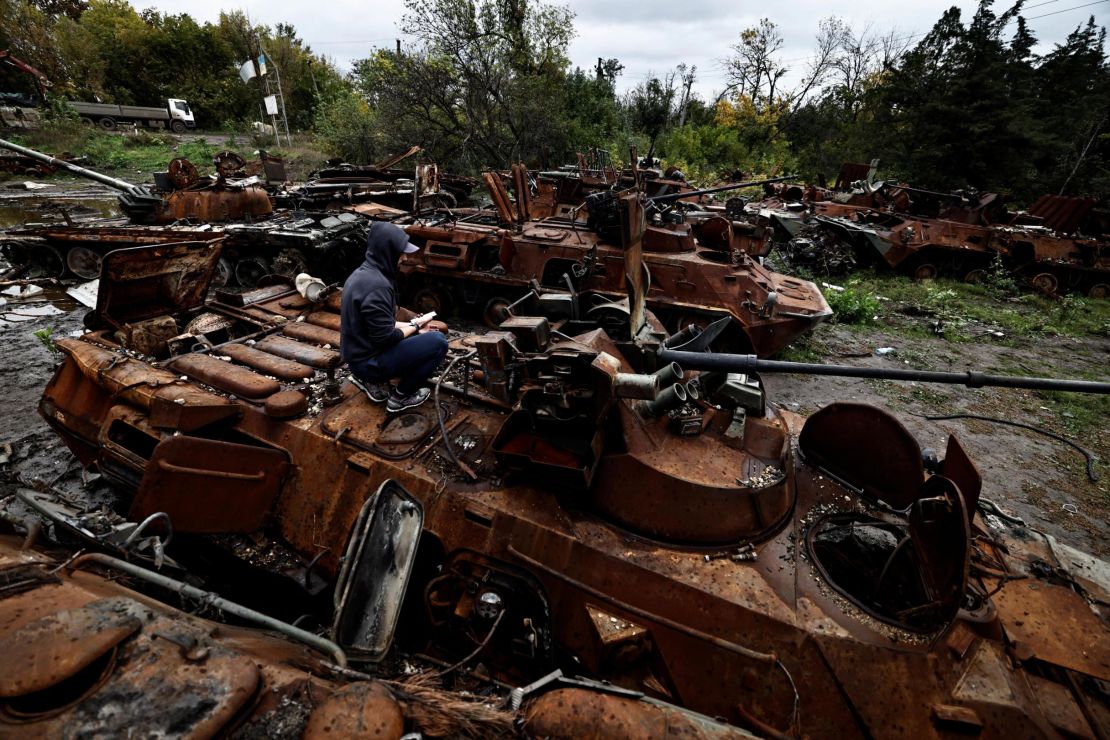 A volunteer uses his mobile phone as he sits on the top of a destroyed Russian armoured vehicle in the recently liberated town of Izium, in Ukraine's northeastern Kharkiv region, on September 27, 2022.