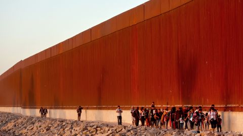 Immigrants walk along the U.S.-Mexico border barrier on their way to await processing by the US Border Patrol after crossing from Mexico on May 21, 2022 in Yuma, Arizona. 