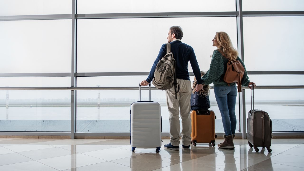 Satisfied man, woman and girl looking out from big window at the airport. They are taking pleasure in airplanes moving along the runway. Copy space in left side