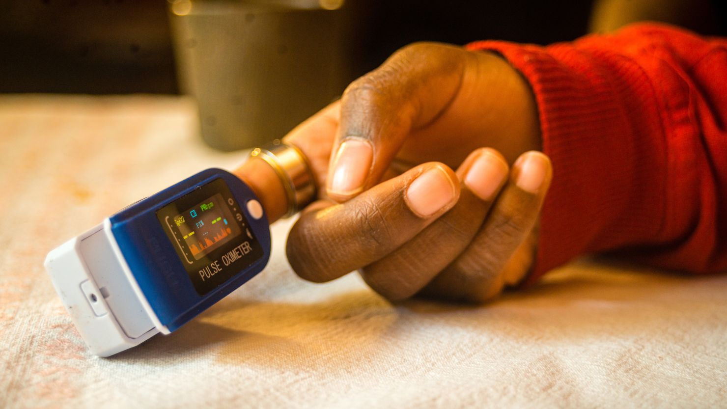 A closeup shot of a pulse oximeter on a black woman's finger to measure pulse rate and oxygen levels