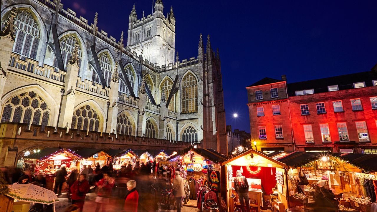 The Christmas Market is illuminated at night behind Bath Abbey.