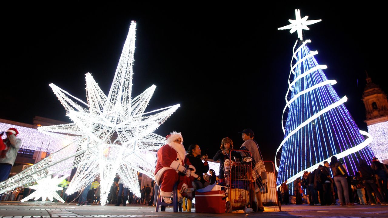 A woman dressed as Santa Claus sits next to a Christmas tree and a Christmas star at Bolivar Square in Bogota.