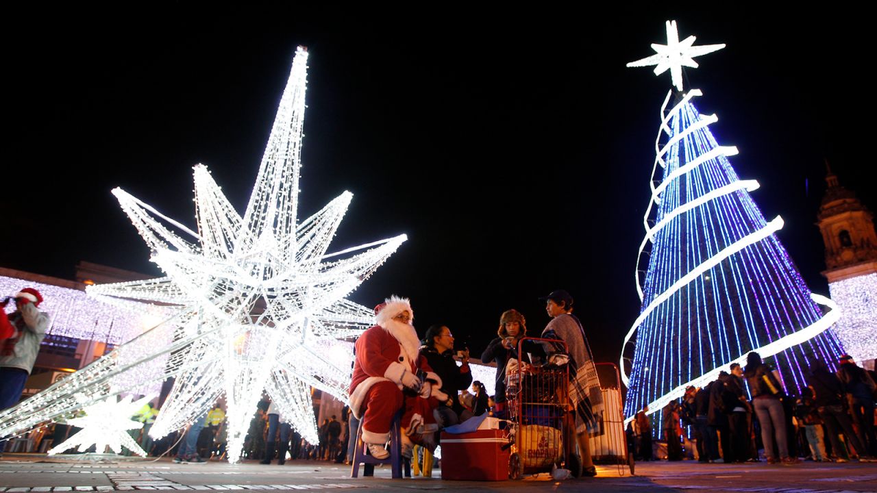A woman dressed as Santa Claus sits next to a Christmas tree and a Christmas star at Bolivar Square in Bogota.