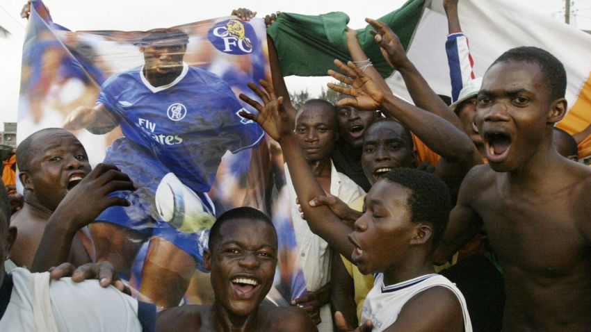 Abidjan, IVORY COAST: Ivorian fans jubilate with a poster of star player Didie Drogba in a street in Koumassi, a poor neighborhood of Abidjan, after Ivory Coast qualified for both World Cup and CAN 2006 competitions 08 Ocotober 2005. AFP PHOTO / KAMPBEL. (Photo credit should read KAMPBEL/AFP via Getty Images)