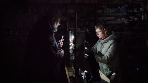 In a pharmacy in Lviv, a man uses the light on his phone to help the pharmacist find products, amid rolling blackouts, on November 16.