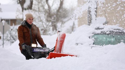 A man in Buffalo uses a snow blower to clear an area around a vehicle.