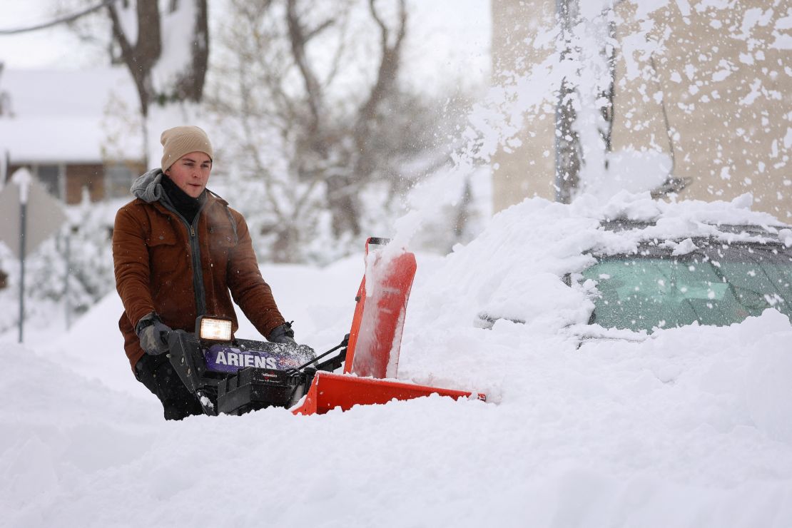 A man in Buffalo uses a snow blower to clear an area around a vehicle.
