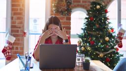 Beautiful woman sitting at the table working with laptop at home around christmas tree rubbing eyes for fatigue and headache, sleepy and tired expression. Vision problem