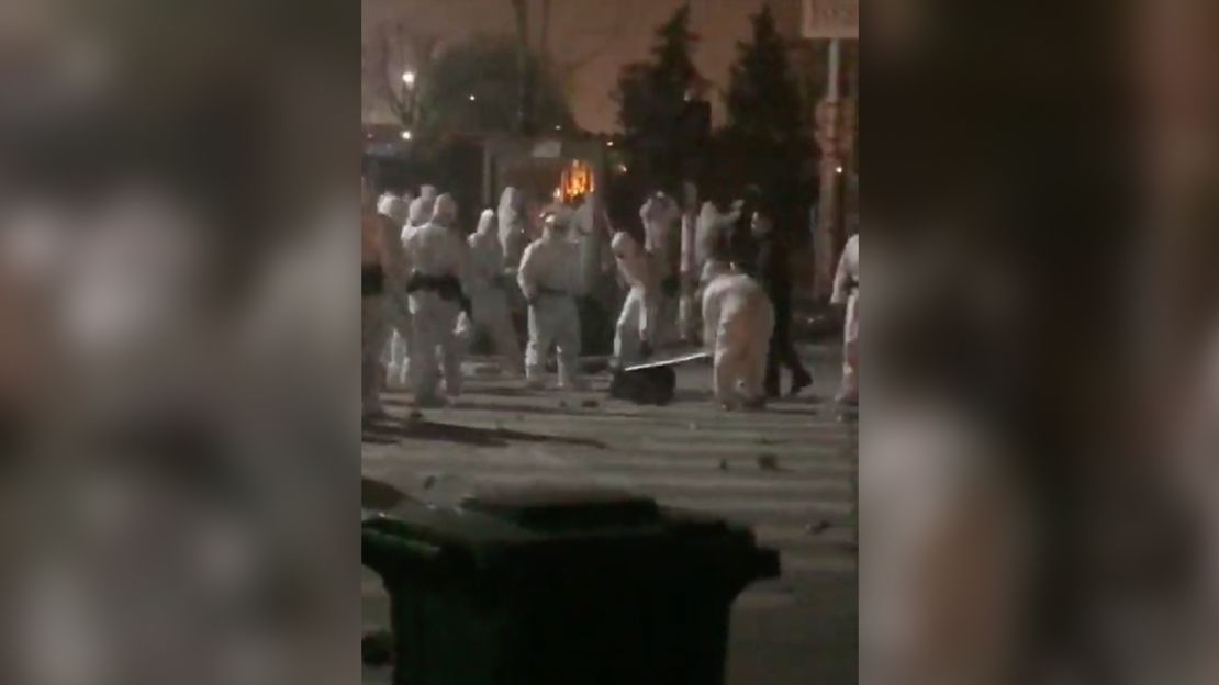 A group of security officers clad in hazmat suits kick and beat a worker lying on the ground. 