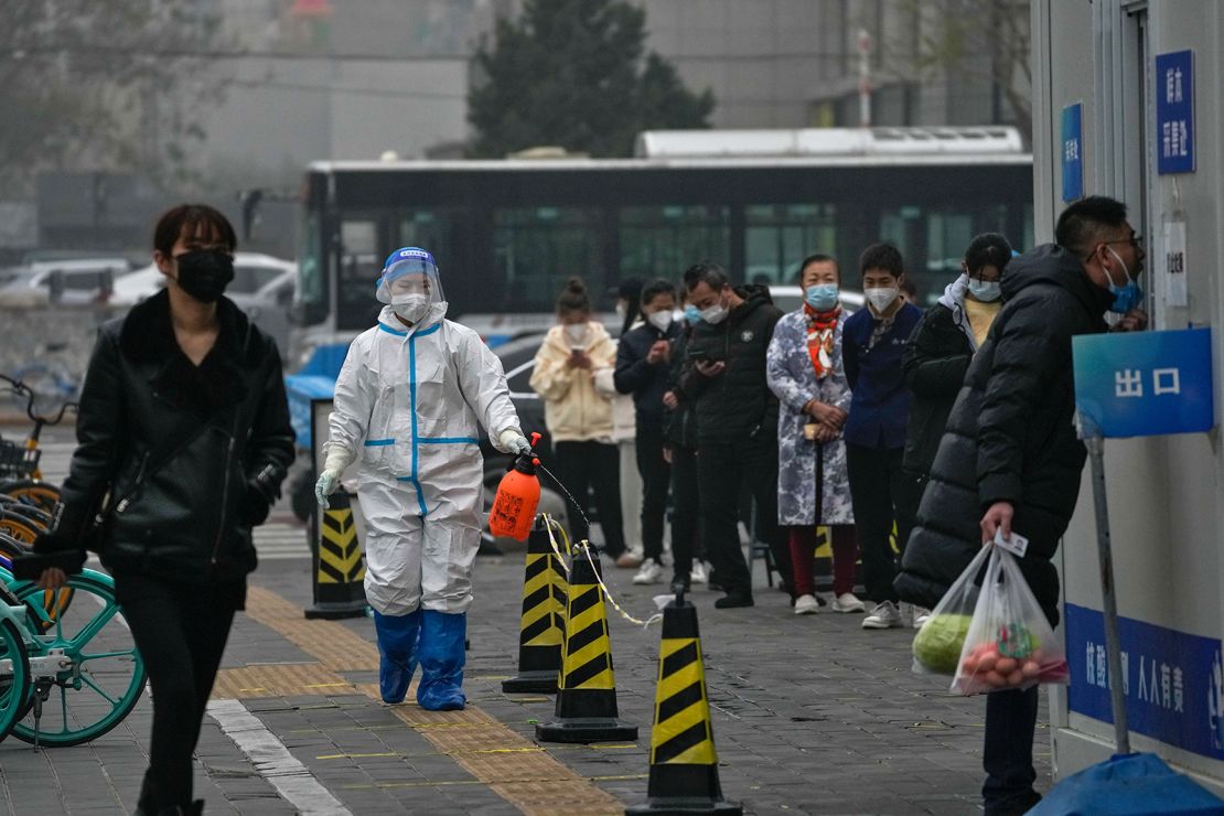 A worker in a protective suit sprays disinfectant as residents stand in line for their routine Covid-19 tests at a coronavirus testing site in Beijing on Thursday, November 24, 2022. 
