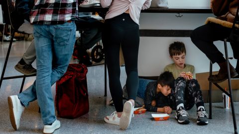 Kids sit on the floor to eat lunch as tables fill up at the mall's packed food court.