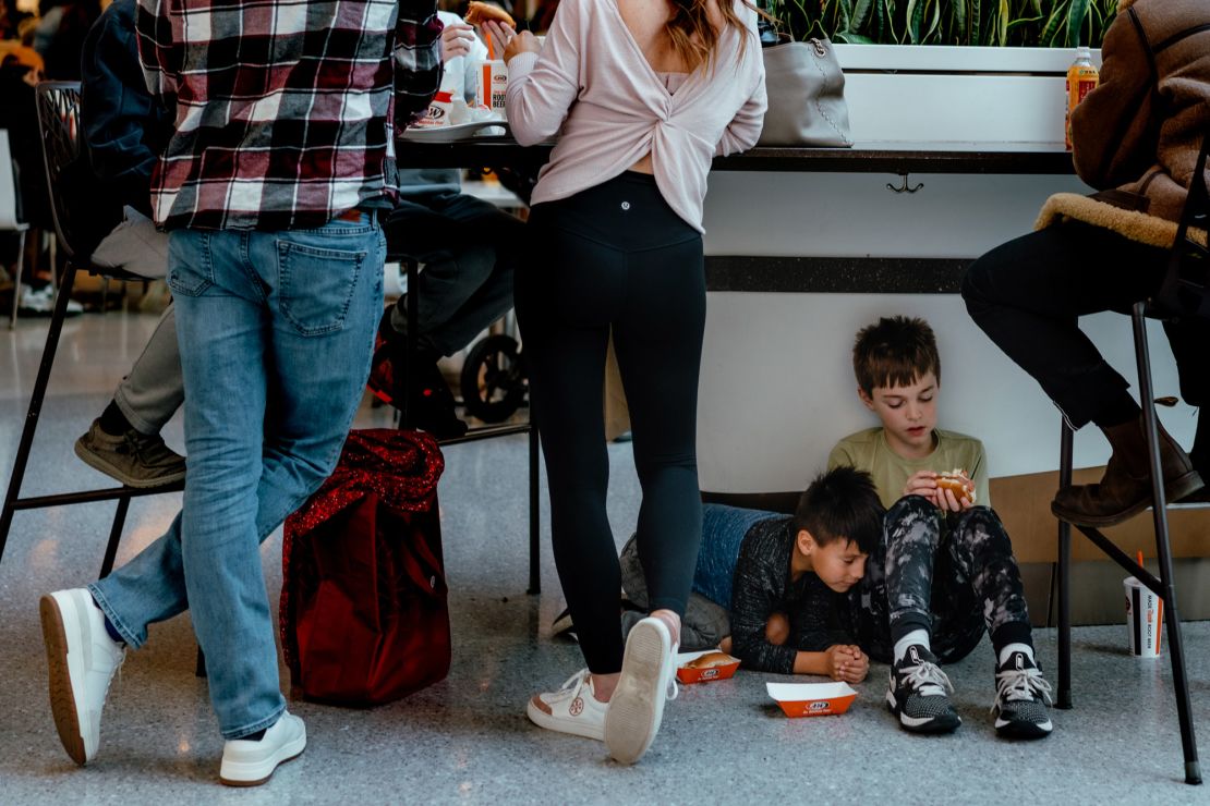 Kids sit on the floor to eat lunch as tables fill up at the mall's packed food court.