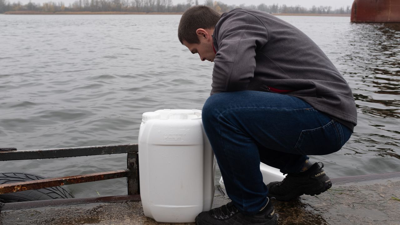 A man fills containers with water from the Dnipro River, with Russian-controlled territory just on the other side of the waterway.