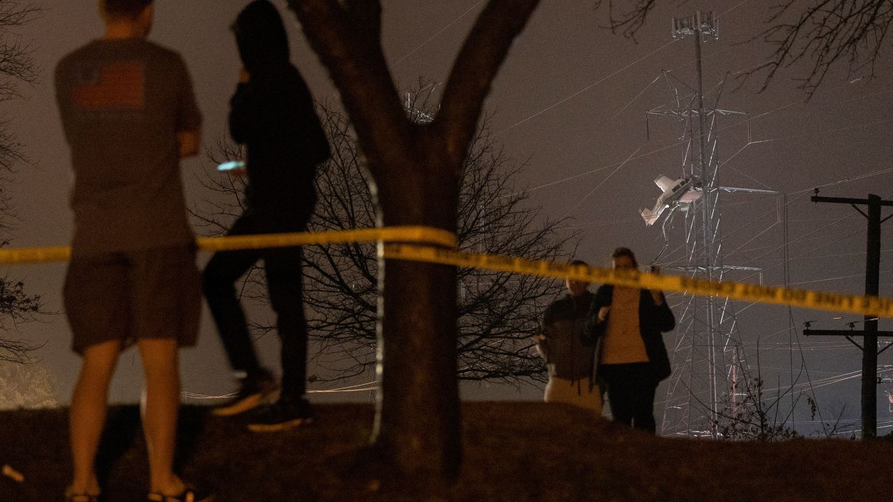 People observe a small plane resting on live power lines after crashing Sunday, November 27, 2022, in Montgomery Village, a northern suburb of Gaithersburg, Maryland.