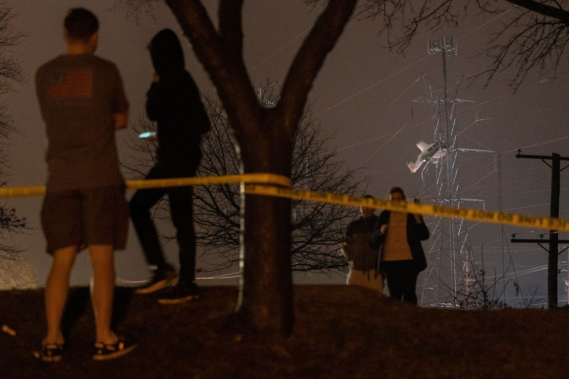 People observe a small plane resting on live power lines after crashing Sunday, November 27, 2022, in Montgomery Village, a northern suburb of Gaithersburg, Maryland.