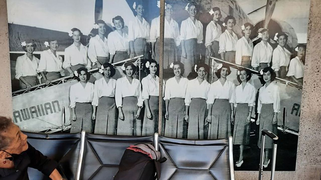 Gwendolyn Bruhn pictured at Daniel K. Inouye International Airport in Honolulu, Hawaii earlier in 2022. Bruhn is looking at a photo of herself (she's top right) taken during her time working for Hawaiian Airlines.