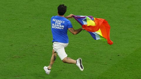 A pitch invader runs onto the pitch wearing a t-shirt with a message saying: 'Respect for Iranian Woman' on the back and holding a rainbow flag.