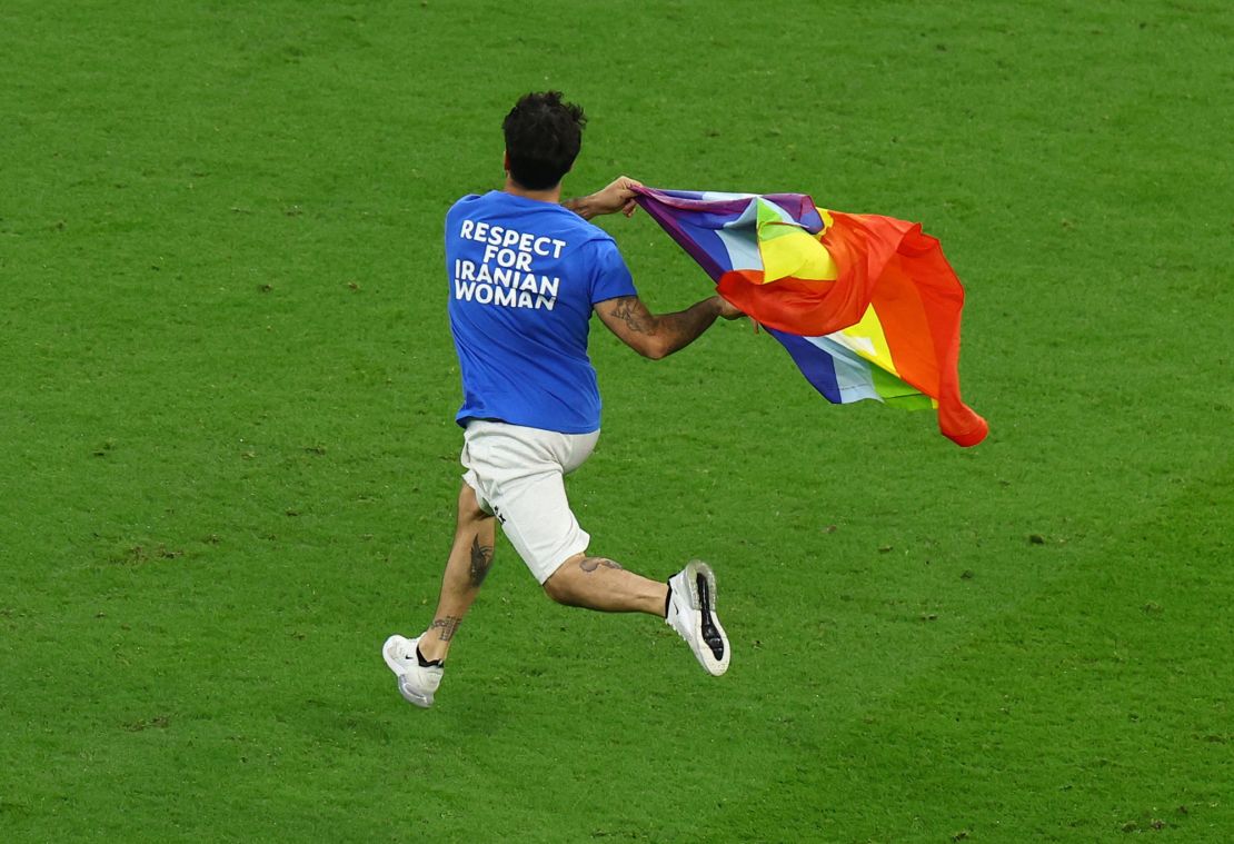 A pitch invader runs onto the pitch wearing a t-shirt with a message saying: 'Respect for Iranian Woman' on the back and holding a rainbow flag.