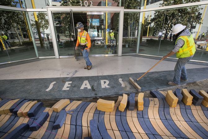 Cesar Villasenor, right, sweeps away dirt in front of a vacant Sears store in Santa Monica, California, in 2020. The location underwent a $50 million makeover to turn the Art Deco-style building into an office, restaurant and retail complex.