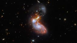 A merging galaxy pair cavort in this image captured by the NASA/ESA/CSA James Webb Space Telescope. This pair of galaxies, known to astronomers as II ZW 96, is roughly 500 million light-years from Earth and lies in the constellation Delphinus, close to the celestial equator. As well as the wild swirl of the merging galaxies, a menagerie of background galaxies are dotted throughout the image.The two galaxies are in the process of merging and as a result have a chaotic, disturbed shape. The bright cores of the two galaxies are connected by bright tendrils of star-forming regions, and the spiral arms of the lower galaxy have been twisted out of shape by the gravitational perturbation of the galaxy merger. It is these star-forming regions that made II ZW 96 such a tempting target for Webb; the galaxy pair is particularly bright at infrared wavelengths thanks to the presence of the star formation. This observation is from a collection of Webb measurements delving into the details of galactic evolution, in particular in nearby Luminous Infrared Galaxies such as II ZW 96. These galaxies, as the name suggests, are particularly bright at infrared wavelengths, with luminosities more than 100 billion times that of the Sun. An international team of astronomers proposed a study of complex galactic ecosystems — including the merging galaxies in II ZW 96 — to put Webb through its paces soon after the telescope was commissioned. Their chosen targets have already been observed with ground-based telescopes and the NASA/ESA Hubble Space Telescope, which will provide astronomers with insights into Webb's ability to unravel the details of complex galactic environments. Webb captured this merging galaxy pair with a pair of its cutting-edge instruments; NIRCam — the Near-InfraRed Camera — and MIRI, the Mid-InfraRed Instrument. If you are interested in exploring the differences between Hubble and Webb's observations of II ZW 96, you can do so here.MIRI was contributed by ESA an