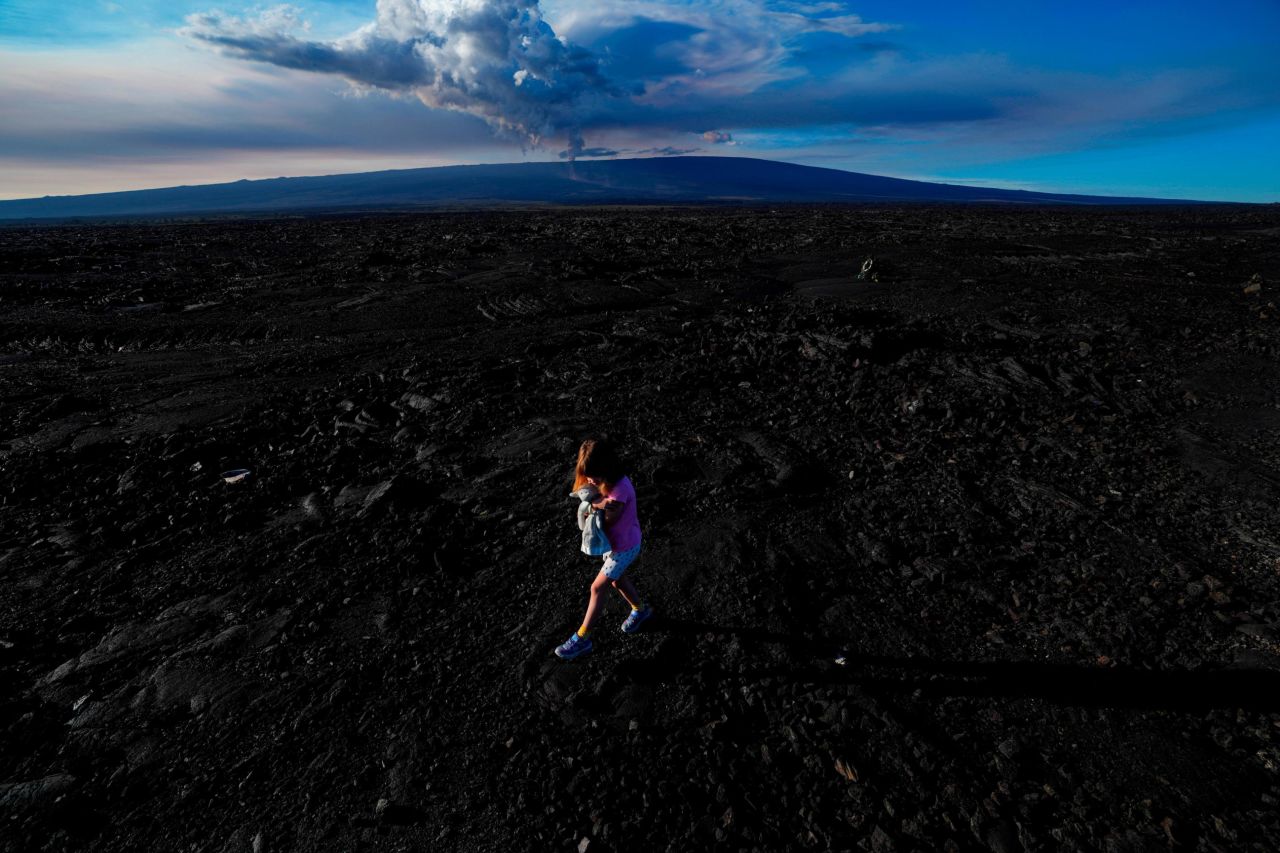 A child holds a stuffed animal while walking over hardened lava rock from a previous eruption.