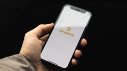 Man hold smartphone with Binance crypto app for buying bitcoin and other cryptocurrency, black background with application logotype